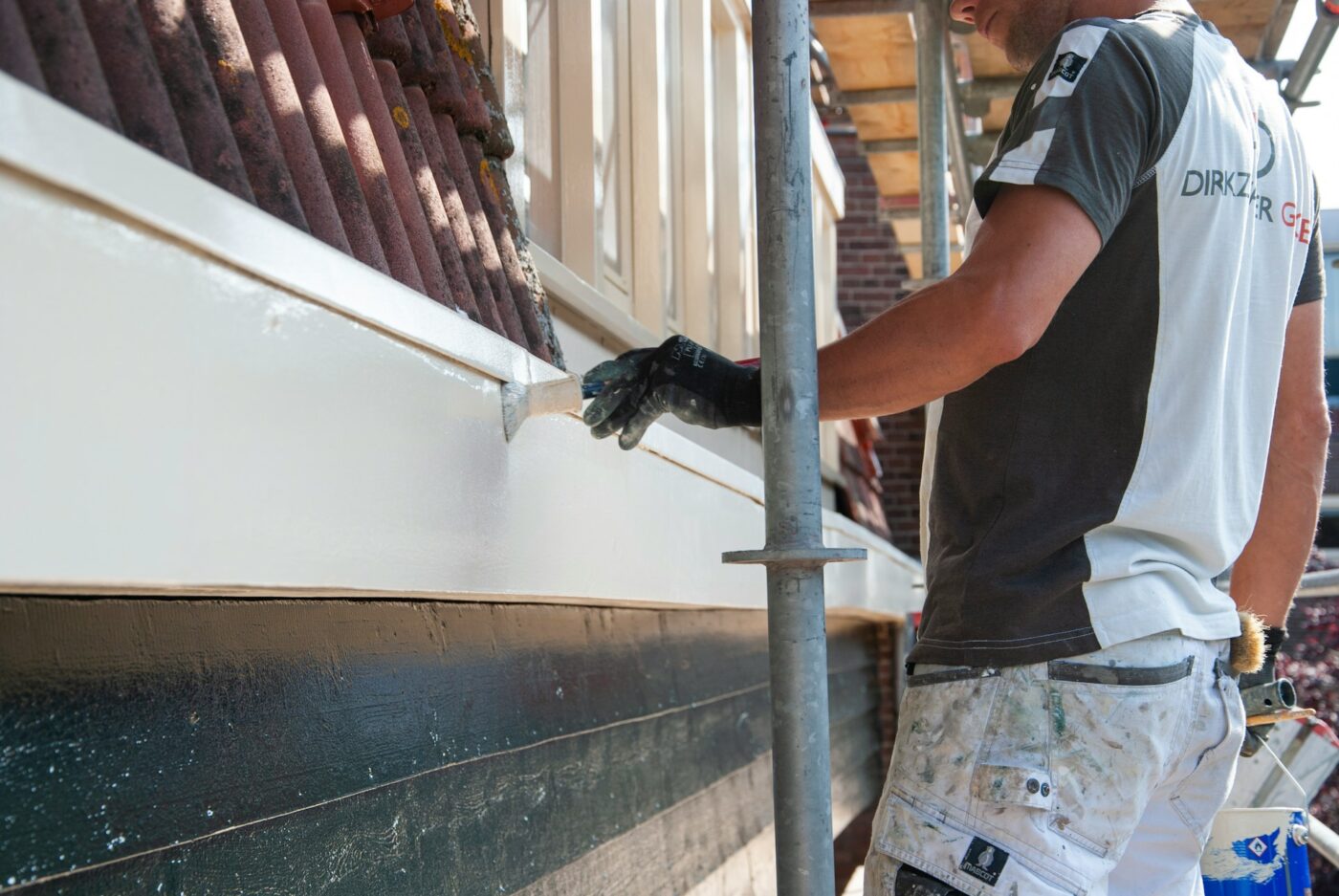 Professional painter applying white exterior trim paint along a building facade while working from scaffolding.